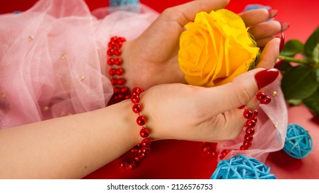 From above of crop anonymous woman with red beads and with red manicure holding a yellow rose on red background in studio with decorative wicker balls. - Shutterstock ID 2126576753