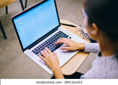 From Above Of Crop Anonymous Woman Using Computer For Doing Task While Sitting At Wooden Table And Looking At Screen