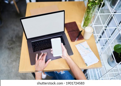 From Above Crop Unrecognizable Female In Ripped Jeans Working On Netbook And Showing Mobile Phone With Empty Screen While Sitting At Desk With Map