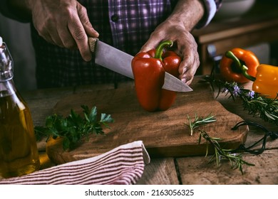 From above of crop unrecognizable man in casual clothes cutting fresh healthy red bell pepper on wooden board standing at table with scattered herbs and bottle of olive oil - Powered by Shutterstock