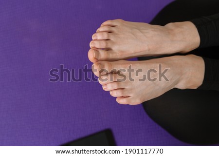 From above of crop unrecognizable woman with bare feet lying on mat in yoga pose and practicing asana at home 