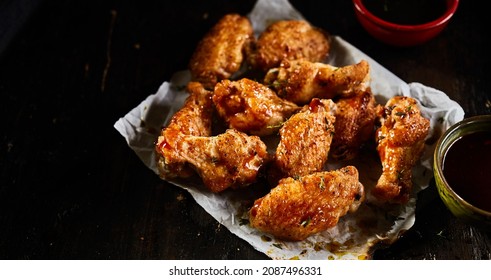 From above of delicious barbeque chicken wings on plate and soy sauce in bowls placed on black background - Shutterstock ID 2087496331