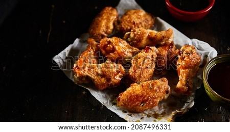 From above of delicious barbeque chicken wings on plate and soy sauce in bowls placed on black background