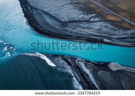 Above of dramatic landscape of glacier river melting flowing through volcanic black sand beach into Atlantic ocean in summer at highlands of Iceland