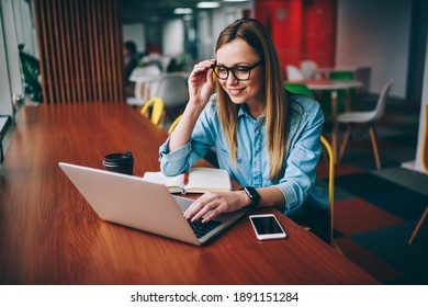 From above of female freelancer with toothy smile looking at screen of laptop while sitting at table and doing work - Powered by Shutterstock