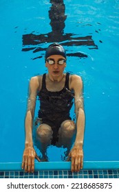 From Above Of Focused Professional Female Swimmer Getting Ready To Start From Swimming Block While Preparing For Backstroke Race During Competition In Swimming Pool 