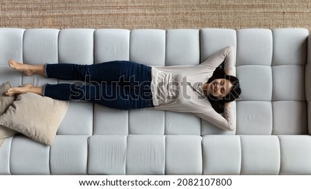 Above full-length view attractive smiling Asian woman lying down with eyes closed put hands behind head relax on cozy sofa, breath fresh ventilated conditioned air enjoy carefree day off alone at home