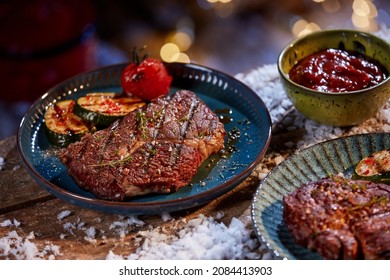 From above of grilled beef steaks with tomatoes and zucchini served on plates on wooden table with snow for winter barbeque
