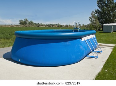 An Above Ground Pool Sets On A Concrete Pad In The Backyard On A Sunny Summer Day.