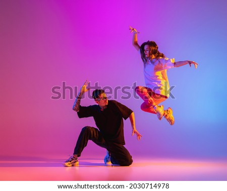 Above the ground. Two young people, guy and girl, dancing contemporary dance over pink background in neon light. Modern dance aesthetics concept