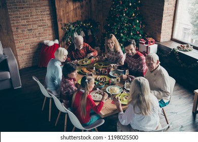 Above High Angle View Of Noel Evening Family Gathering. Cheerful Grey-haired Grandparents, Brother, Sister, Son, Daughter At House Feast Party, Sitting At Homemade Lunch Table, Talking, Fir Tree