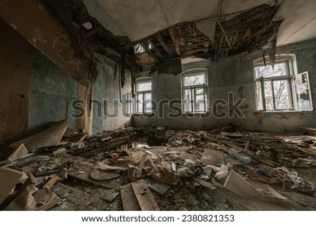 From above of interior of spacious hall with glass windows and heap of rubble with damaged furniture on floor with hole while destroyed decoration of ceiling with damaged hanging planks in daylight