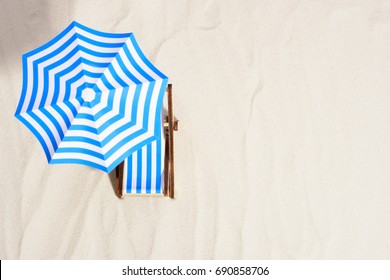 From Above Of Lounge Area On Beach With Striped Chair Under Umbrella.