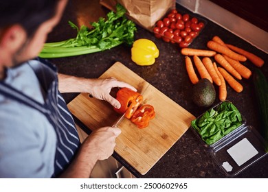 Above, man and cutting with vegetables for health, nutrition or vegan diet for wellness. Male chef, groceries and wood board in kitchen for cooking with food and culinary hobby to prepare home dinner - Powered by Shutterstock