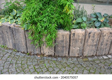 above the palisade of wooden sleepers are planted ornamental perennials and a very nice dwarf bamboo. arch by the road made of cobblestones - Shutterstock ID 2040575057