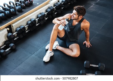 Above Photo Of Fitness Man Sitting In Gym. With Bottle And Weight