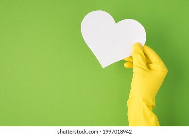 Above photo of hands in yellow gloves with empty card as heart isolated on the green background