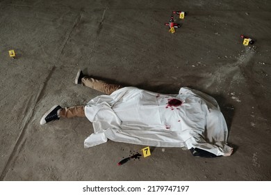 Above Shot Of Dead Body Of Murdered Man Covered With White Sheet Lying On Asphalt Of Parking Area Or Some Other Outdoor Place