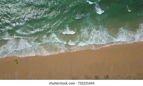 From above shot taken with drone showing green wave of ocean running on sand of tropical beach creating splashes and foam.