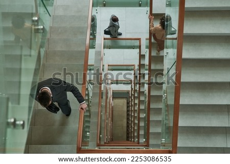 Above shot of three business people in formalwear walking upstairs and between staircases inside modern building while going to work