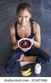 Above shot of a woman with a bowl of berries wearing a sportive outfit staring at the camera.