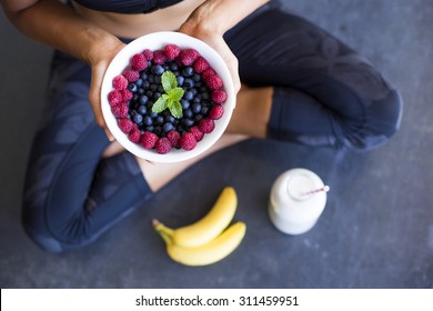 Above shot of a woman with a bowl of berries, a bottle of almond milk and two bananas wearing a sportive outfit.