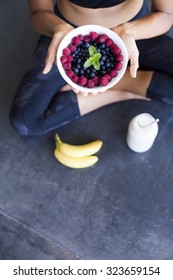 Above shot of a woman with a bowl of berries, a bottle of almond milk and two bananas wearing a sportive outfit. - Shutterstock ID 323659154