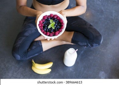 Above shot of a woman with a bowl of berries, a bottle of almond milk and two bananas wearing a sportive outfit. non-diary