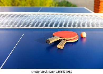 From Above Of Similar Red Ping Pong Paddles And Small Ball On Blue Table On Sunny Summer Day