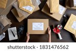 Above table top view of female warehouse worker or seller packing ecommerce shipping order box for dispatching, preparing post courier delivery package, dropshipping shipment service concept.