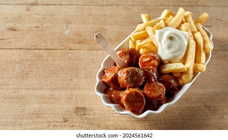 A From Above Of Tasty Curried Sausage Chunks With Hot Chips And Mayonnaise In Bowl With Eco Stick On Brown Background