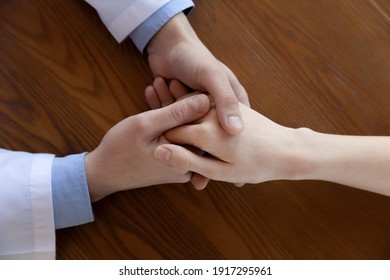 Above Top Close Up View Compassionate Male General Practitioner Holding Hand Of Young Female Patient, Supporting After Getting Bad Laboratory Test Results, Comforting Ot Soothing At Checkup Meeting.