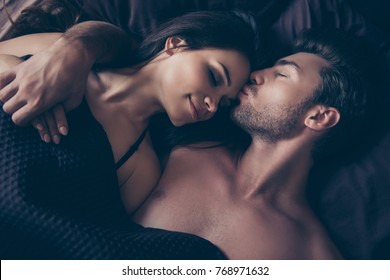 Above top view close up cropped photo of lovely graceful tender cute smiling beautiful sexualcouple, they are hugging under blanket in bed on dark bedsheet, man is kissing gently his woman in forehead