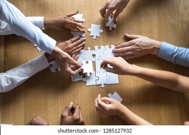 Above top view to the hands of diverse people assembling connecting jigsaw puzzle associates put pieces searching common solutions making right decisions together. Support and help in business concept