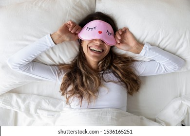 Above top view head shot happy millennial mixed race healthy woman lying in bed with sleeping mask, waking up after sweet dreams. Smiling young relaxed lady feeling energetic in morning at home.