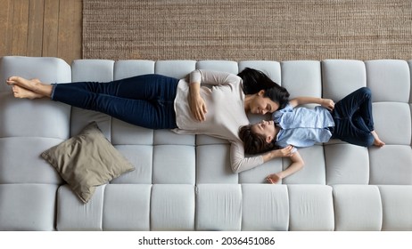 Above top view peaceful young korean asian mother resting on comfortable sofa with smiling adorable little kid son, spending lazy leisure weekend time, daydreaming sleeping napping together at home.