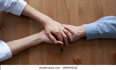Above top view young compassionate female medical worker nurse doctor covering wrinkled hand of older senior patient, giving psychological help or supporting stressed mature retired man at clinic.