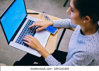 From Above Unrecognizable Female Student Looking At Screen While Doing Task Sitting At Wooden Table And Typing On Laptop Keyboard