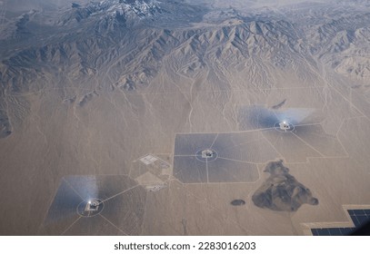 From above, a vast array of solar panels gleams in the sunlight, surrounded by a dessert and bordered by a shimmering lake.