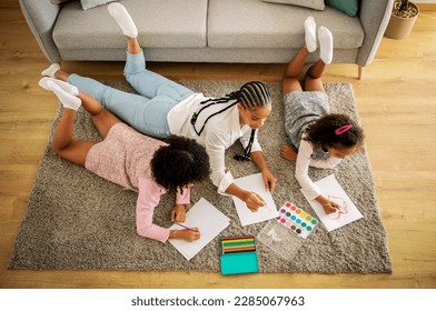 Above View Of African American Family Of Three Drawing And Having Fun Lying On Floor At Home  Mother And Two Daughters Painting Spending Time Together On Weekend  Hobby And Talent