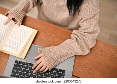 Above view, An Asian female college student doing her homework, working on her research assignment, using laptop computer, looking information on a book. - Shutterstock ID 2203643273