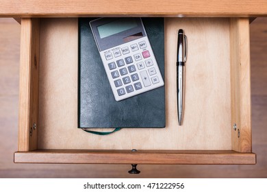 above view of ballpen, calculator and notebook in open drawer of nightstand