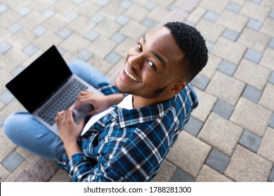 Above View Of Black Man Using Personal Computer Sitting On The Stairs In City, Looking At Camera, Mock Up