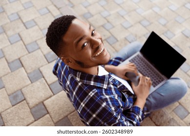 Above view of black man using personal computer sitting on the stairs in city, looking at camera, mock up