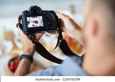 Above view closeup of unrecognizable photographer holding professional photo camera while taking pictures of food on table, copy space - Powered by Shutterstock