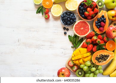 Above view of colorful fruits, strawberries, blueberries, mango, orange, grapefruit, banana, apple, grapes, kiwis on the white background, copy space for text, selective focus