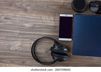 Above View Of Communication Gadgets Isolated On Wooden Table.  Laptop, Headphone, Cell Phone And Mini Speaker.  Noise And Grain Is Visible Due To Low Light. 