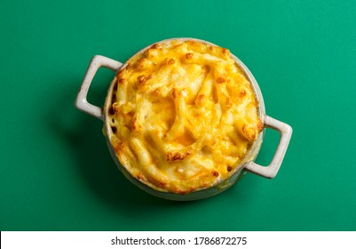 Above view with cooked mac and cheese in a ceramic tray, isolated on a green colored background. Tasty homemade food with macaroni and cheese.