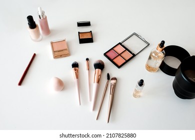 Above View Of Cosmetic Products, Makeup Brushes And Camera Lenses Lying On White Desktop Background. Object Photography Concept. Photo And Beauty Blogging. No People