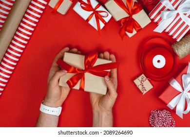 Above View Cropped Image Of Male Hands Holding Gift Box On Red Background. Man Wrapping Gifts For Christmas.